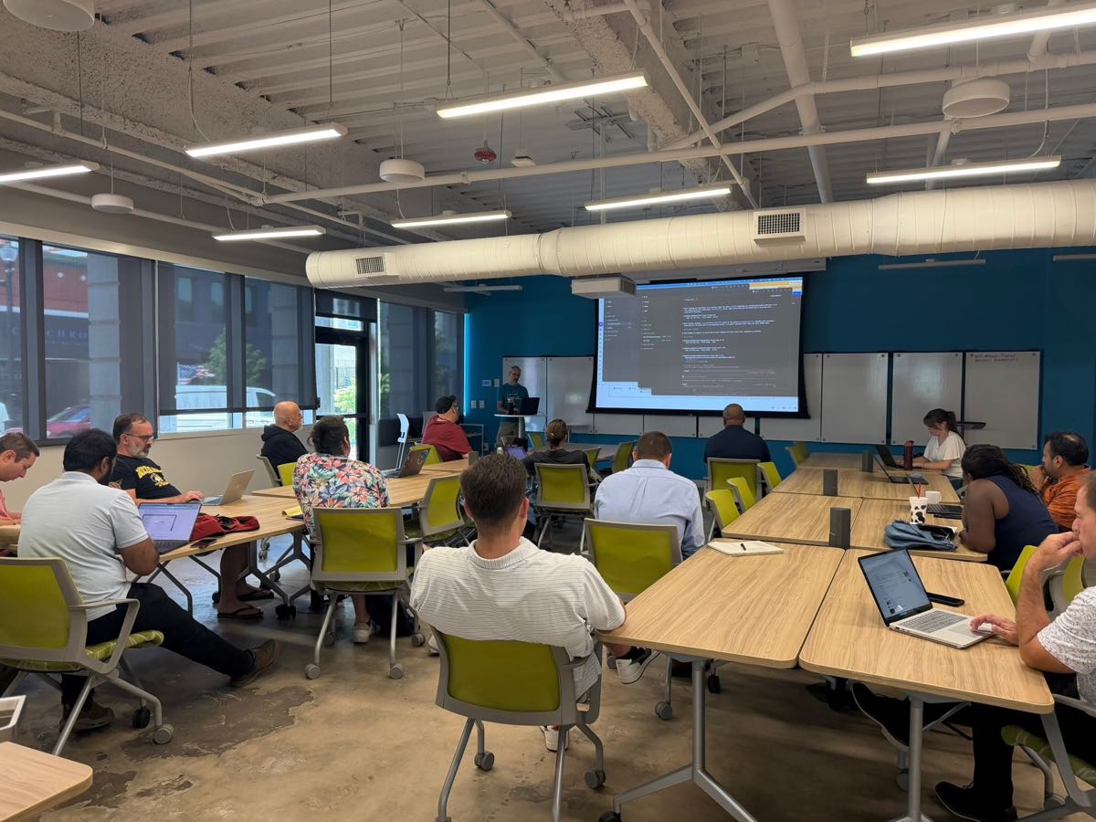A daytime Concord AI Lab session at Flywheel Coworking: attendees with laptops open at long tables while a presenter walks through code on the big screen.