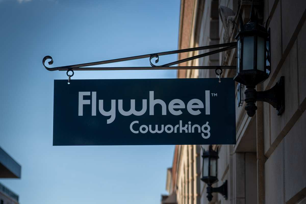 The Flywheel Coworking sign hanging on its wrought-iron bracket above the sidewalk in downtown Concord.