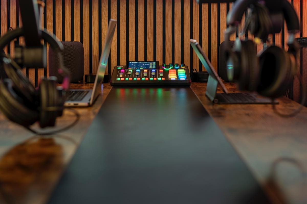 Looking down the recording desk at The Groove Studio — a lit mixing console centered between two laptops, headphones and microphones either side, against a slatted wood wall.